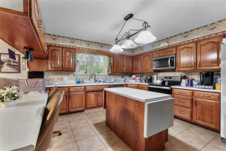 Kitchen featuring stainless steel appliances, tasteful backsplash, light countertops, and brown cabinets