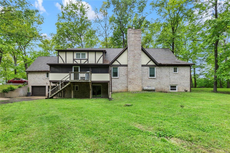 Back of house featuring a garage, a sunroom, a chimney, stairway, and driveway