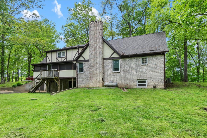 Rear view of property featuring a sunroom, brick siding, a chimney, and a lawn