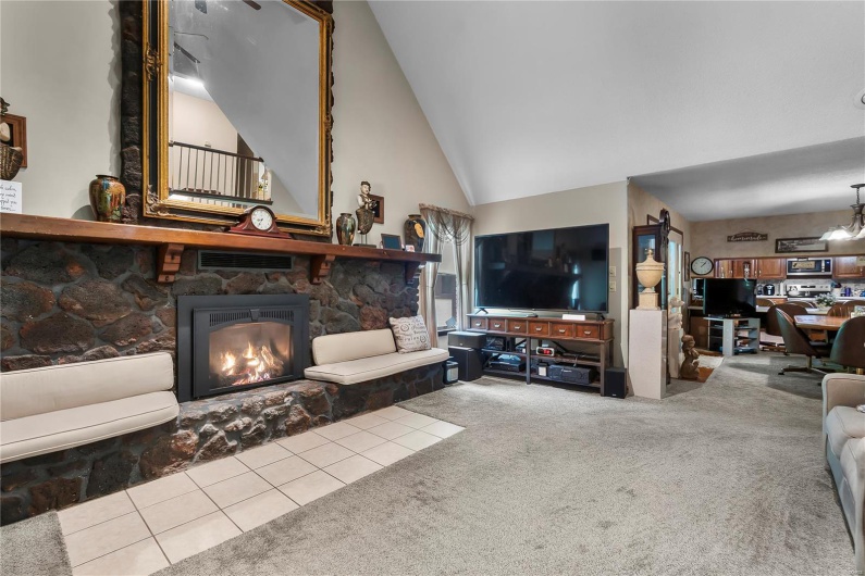 Carpeted living room featuring high vaulted ceiling, a stone fireplace, and tile patterned floors