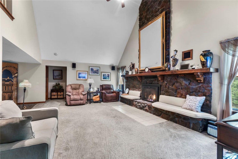Carpeted living room with a fireplace, a ceiling fan, and high vaulted ceiling