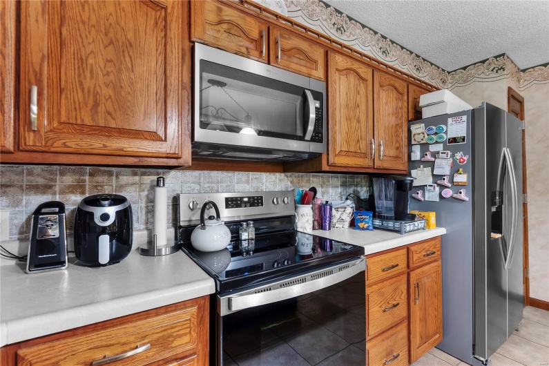 Kitchen with brown cabinetry, light tile patterned floors, decorative backsplash, light countertops, and appliances with stainless steel finishes