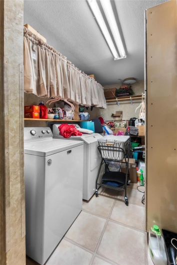 Clothes washing area with laundry area, a textured ceiling, separate washer and dryer, and light tile patterned floors