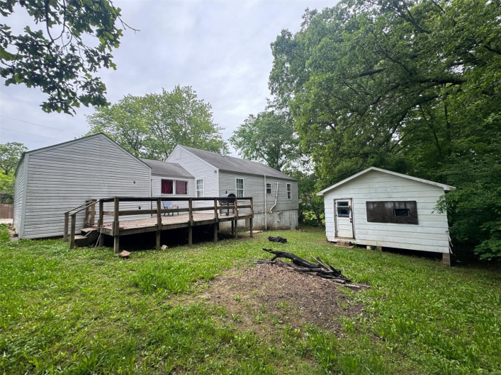 View of green lawn featuring a wooden deck, an outdoor structure, and a storage shed