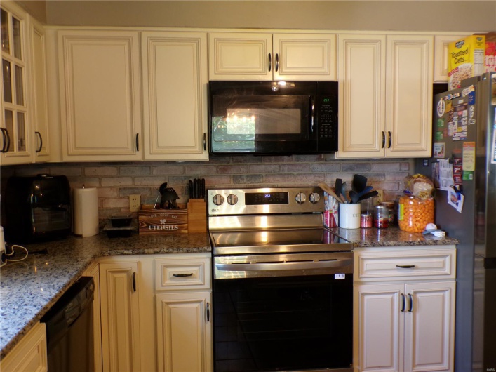 Kitchen featuring black appliances, tasteful backsplash, solid surface counters, and glass insert cabinets