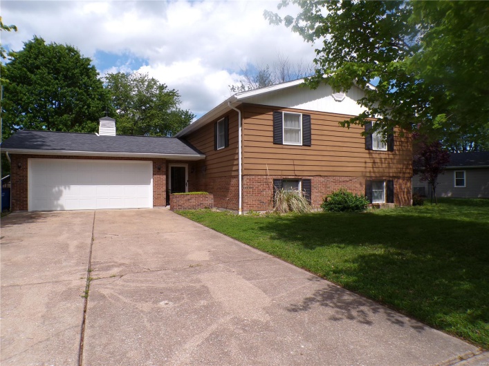 Split level home featuring brick siding, a front yard, driveway, a garage, and a chimney