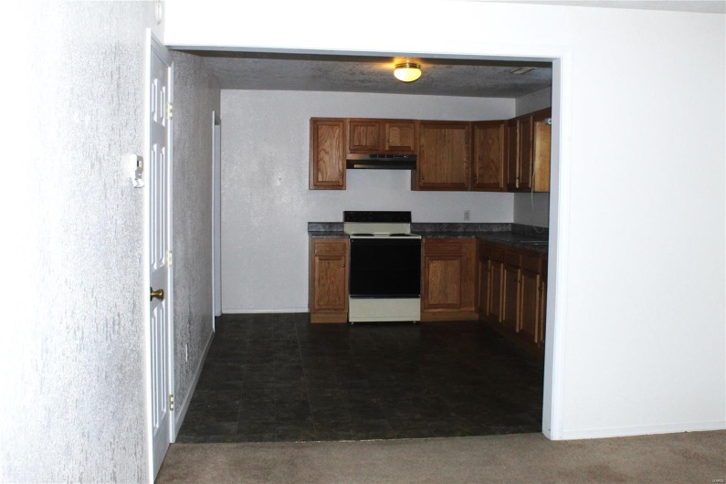 Kitchen featuring under cabinet range hood, dark countertops, electric range oven, and brown cabinetry