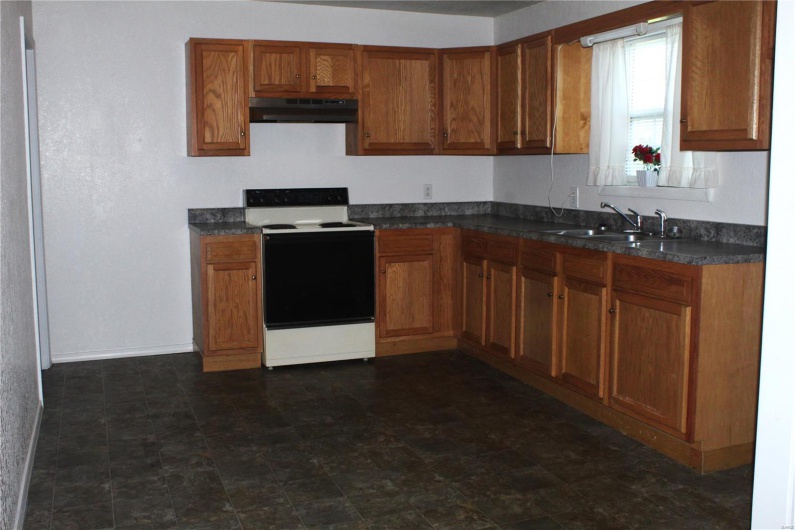 Kitchen featuring under cabinet range hood, dark countertops, brown cabinets, and range with electric stovetop