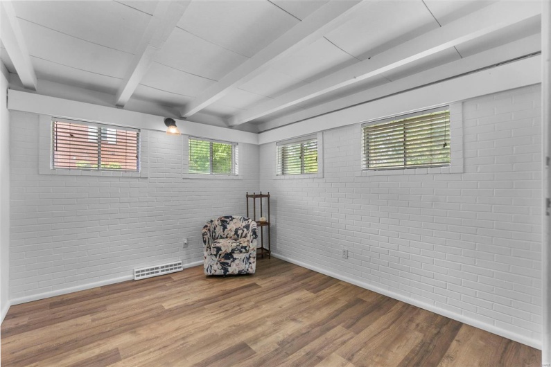 Unfurnished room featuring brick wall, beamed ceiling, wood finished floors, and baseboards