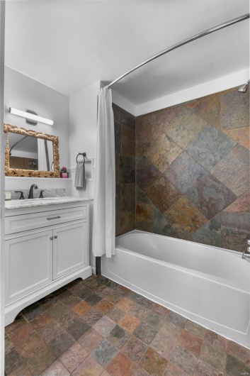 Bathroom with stone tile floors, shower / bath combo, and vanity