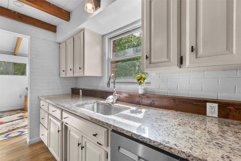 Kitchen with a sink, healthy amount of natural light, light stone counters, wood finished floors, and beamed ceiling