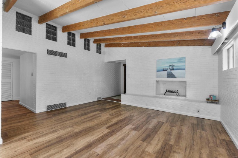 Unfurnished living room featuring wood finished floors, a brick fireplace, baseboards, beamed ceiling, and brick wall