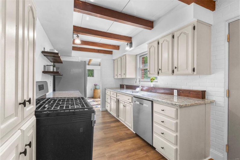 Kitchen with stainless steel appliances, a sink, wood finished floors, tasteful backsplash, and beam ceiling