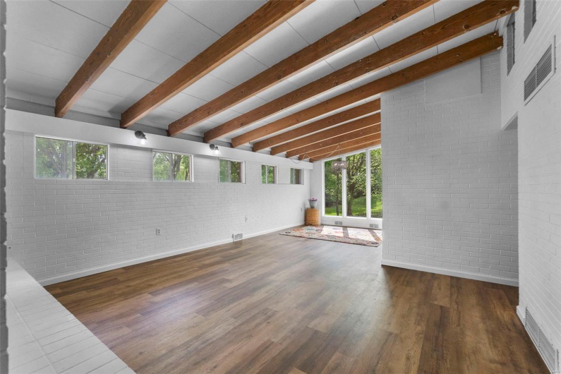 Unfurnished living room featuring plenty of natural light, brick wall, wood finished floors, and baseboards