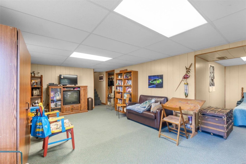 Living room featuring a paneled ceiling, carpet, and wooden walls