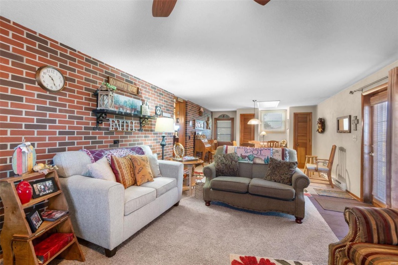 Living room with ceiling fan, brick wall, and carpet