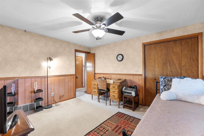 Bedroom featuring light carpet, ceiling fan, a textured ceiling, a closet, and wooden walls
