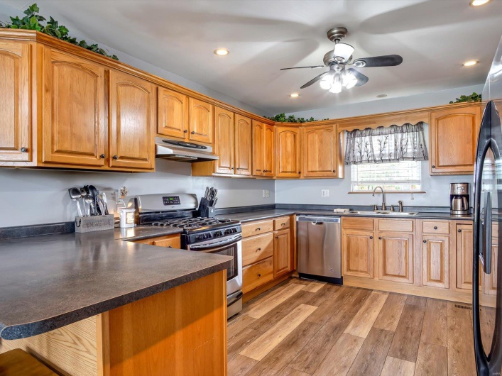 Kitchen with stainless steel appliances, a sink, under cabinet range hood, dark countertops, and a peninsula