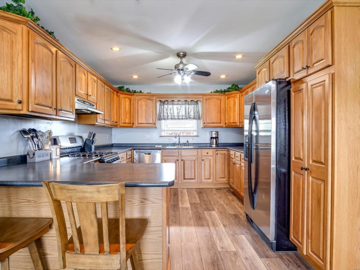 Kitchen featuring stainless steel appliances, under cabinet range hood, a peninsula, a ceiling fan, and light wood finished floors