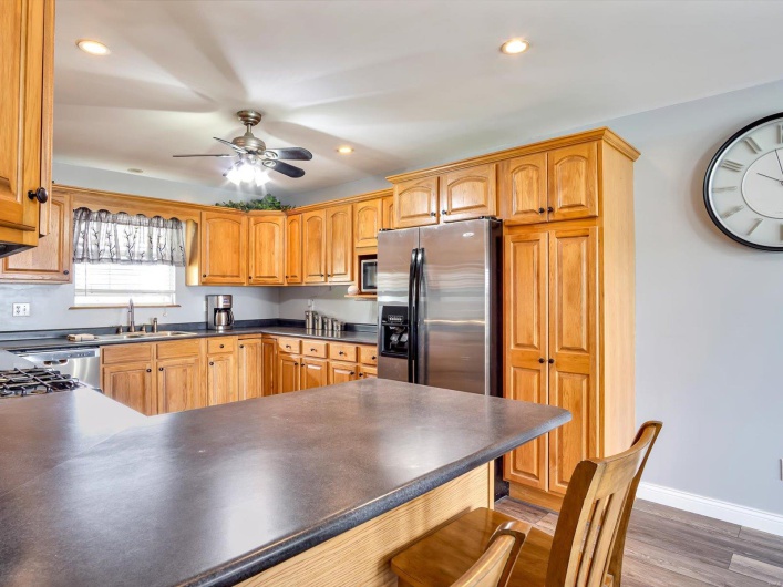 Kitchen with a sink, dark countertops, ceiling fan, a kitchen bar, and baseboards