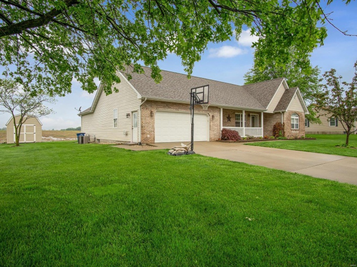 Ranch-style home with a storage unit, a shingled roof, an attached garage, a front lawn, and brick siding