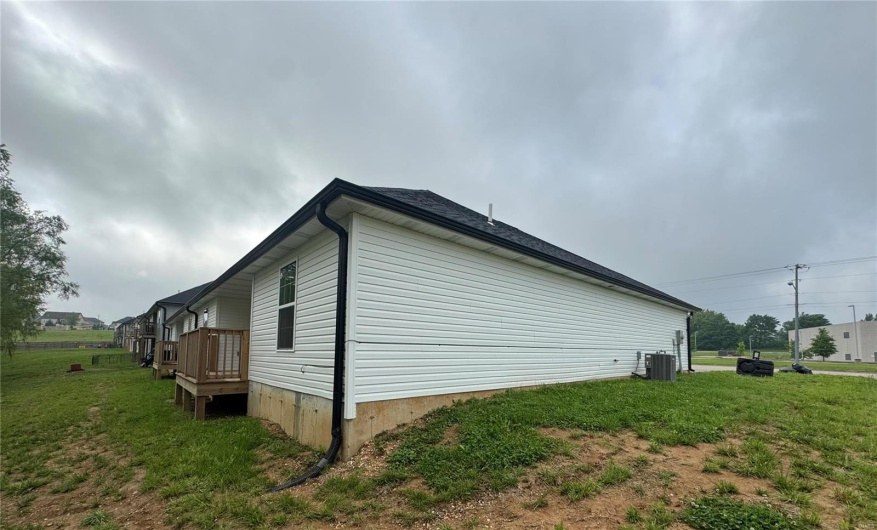 View of side of home featuring a deck, central air condition unit, and a lawn