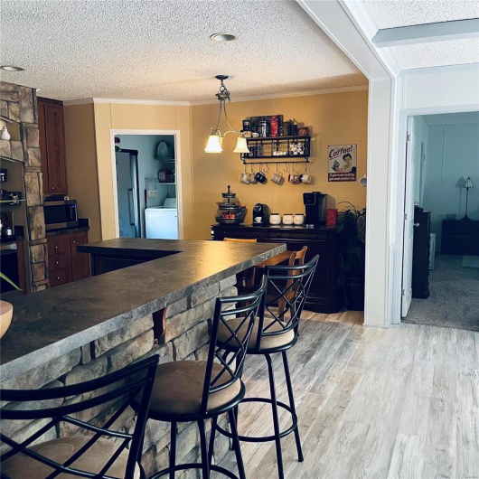 Indoor dry bar with stainless steel microwave, a textured ceiling, ornamental molding, washer / dryer, and light wood finished floors