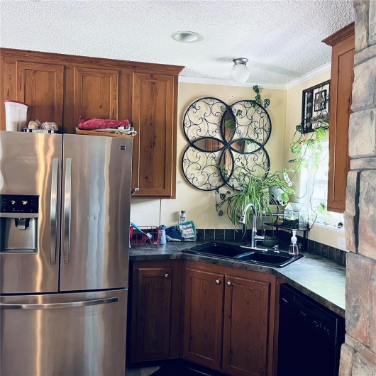 Kitchen with stainless steel fridge, black dishwasher, a sink, dark countertops, and a textured ceiling