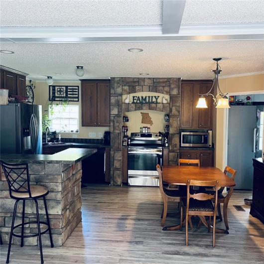 Kitchen with stainless steel appliances, a textured ceiling, dark brown cabinetry, crown molding, and a kitchen bar