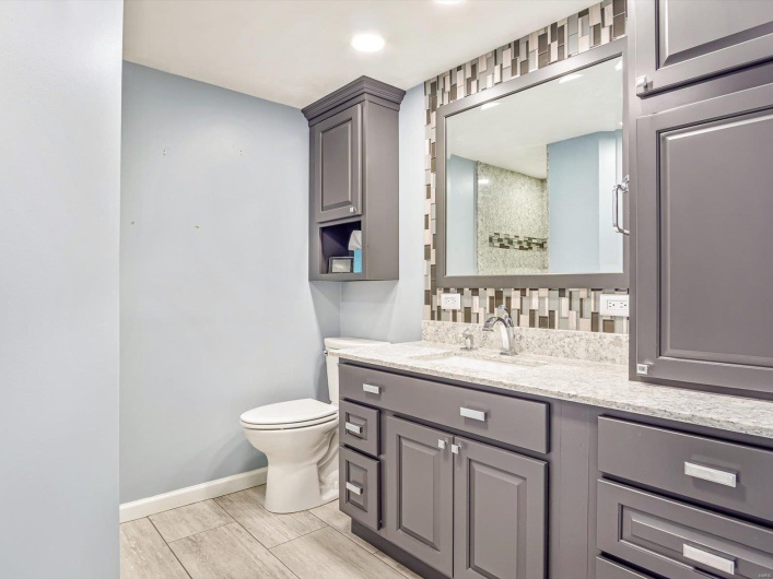 Bathroom featuring toilet, vanity, wood finish floors, baseboards, and a shower