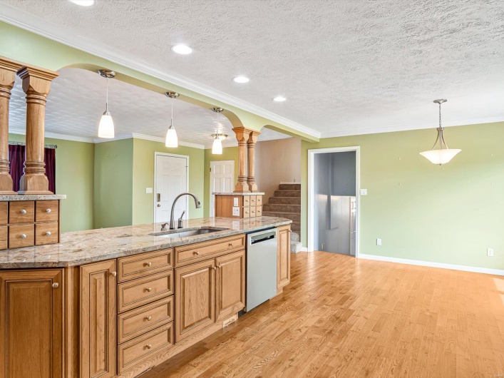 Kitchen with dishwasher, a sink, decorative columns, light wood-style flooring, and a textured ceiling