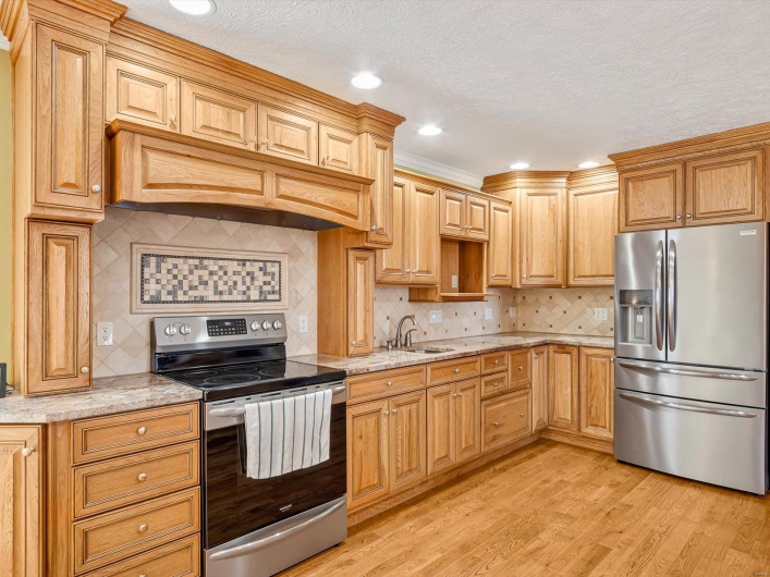 Kitchen featuring appliances with stainless steel finishes, light wood-style floors, tasteful backsplash, light stone counters, and a sink