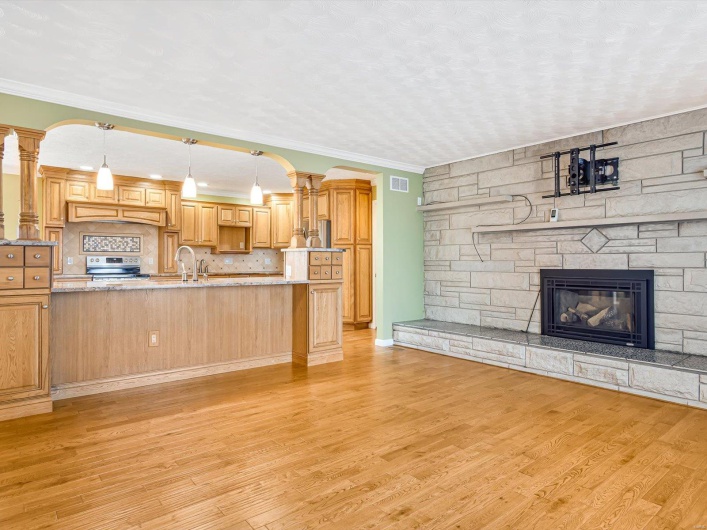 Unfurnished living room featuring light wood finished floors, a fireplace, ornamental molding, decorative columns, and arched walkways