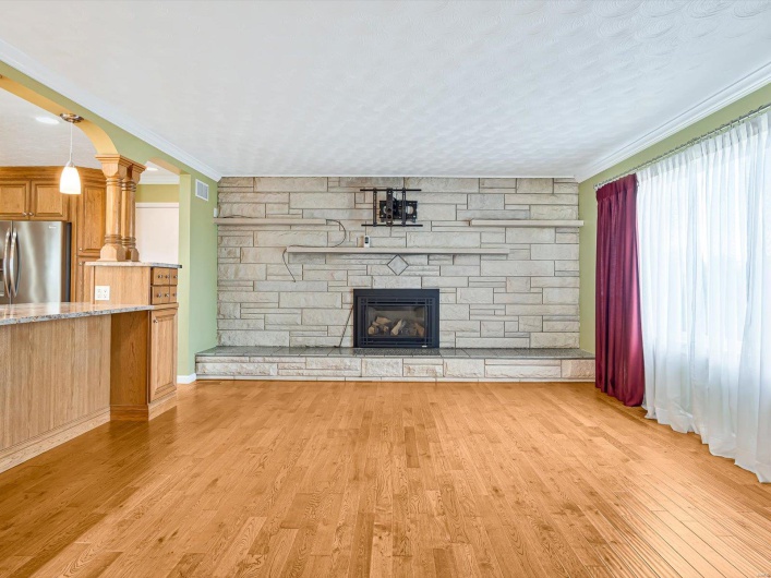 Unfurnished living room featuring a stone fireplace, light wood-style flooring, ornamental molding, and decorative columns