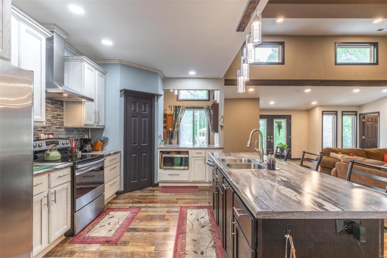 Kitchen with stainless steel appliances, wall chimney range hood, a sink, a kitchen island with sink, and wood finished floors
