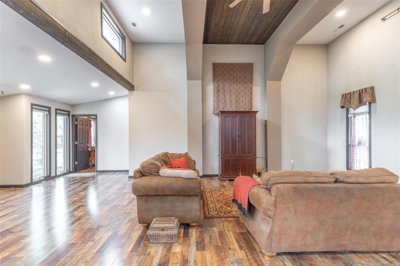 Living area with healthy amount of natural light, hardwood / wood-style flooring, ceiling fan, recessed lighting, and a towering ceiling