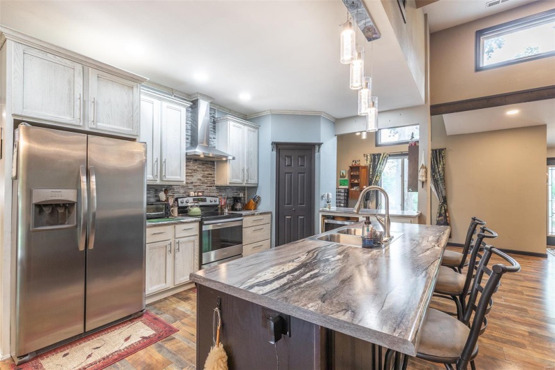 Kitchen with stainless steel appliances, wall chimney exhaust hood, a sink, backsplash, and light wood-style flooring