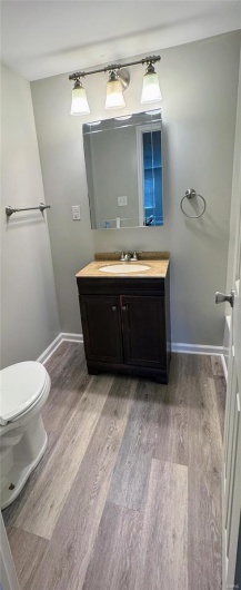 Bathroom featuring wood finished floors, vanity, toilet, and baseboards