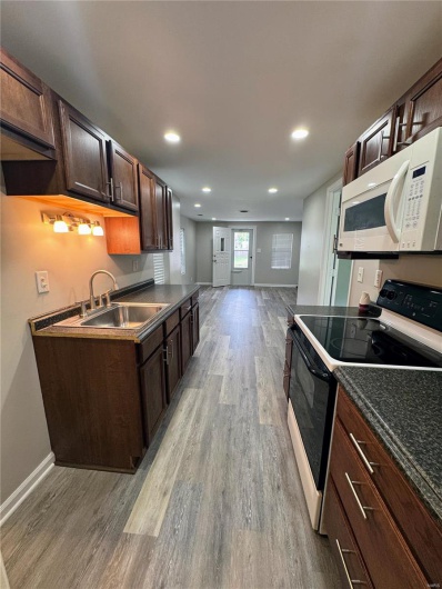 Kitchen with white microwave, electric range, light wood-type flooring, a sink, and dark countertops