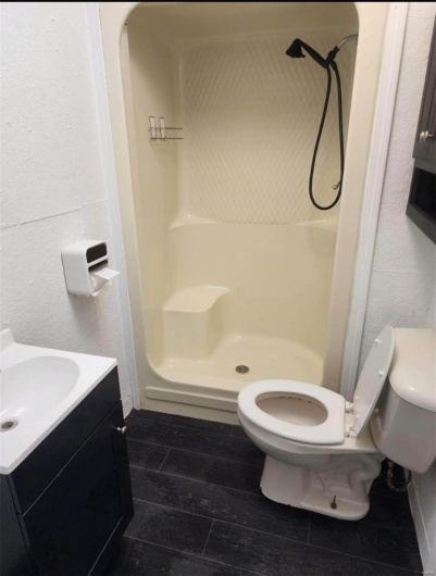 Full bathroom featuring a stall shower, toilet, and wood finished floors