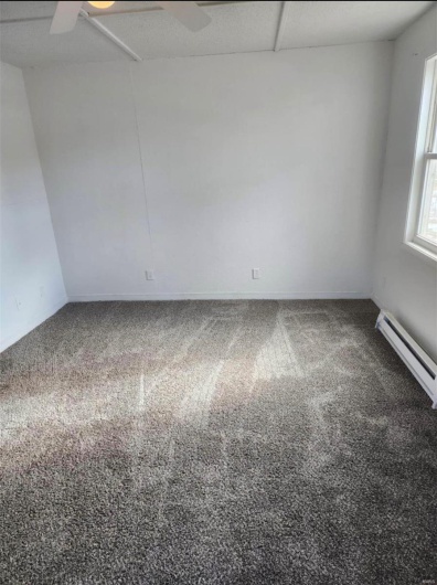 Carpeted empty room with a ceiling fan, baseboard heating, and baseboards