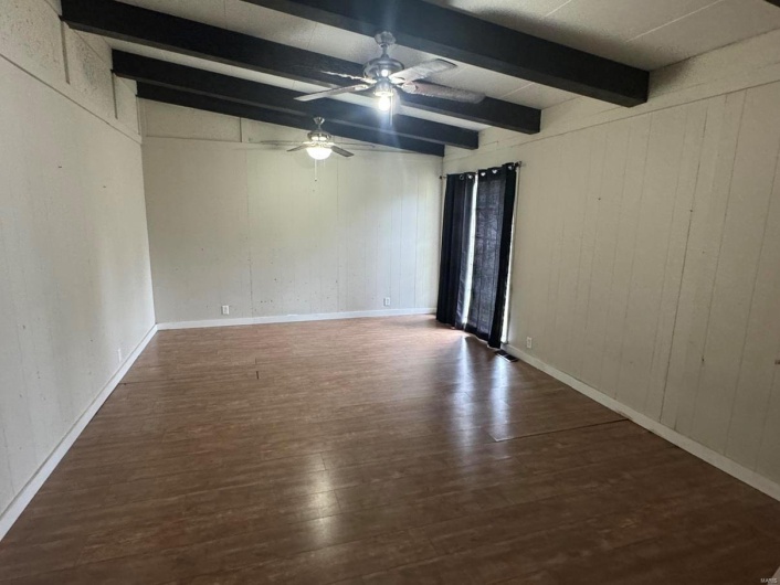 Empty room featuring beamed ceiling, a ceiling fan, wood finished floors, and wood walls
