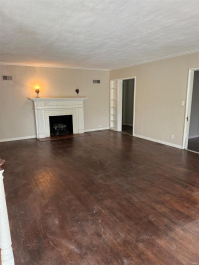 Unfurnished living room featuring wood-type flooring, crown molding, a brick fireplace, a textured ceiling, and baseboards