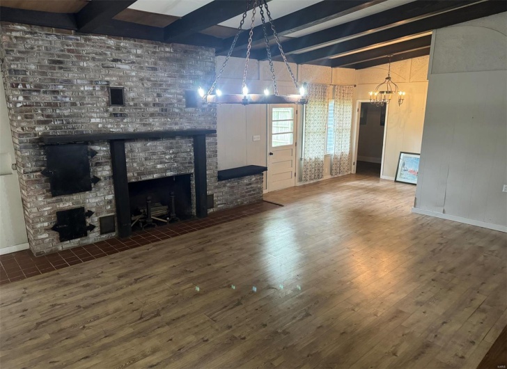 Unfurnished living room featuring a fireplace, a chandelier, wood finished floors, beam ceiling, and baseboards