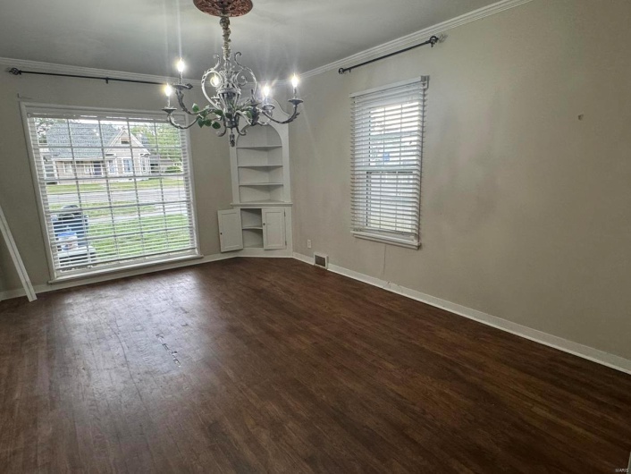 Unfurnished dining area featuring a chandelier, ornamental molding, dark wood-style floors, built in features, and baseboards
