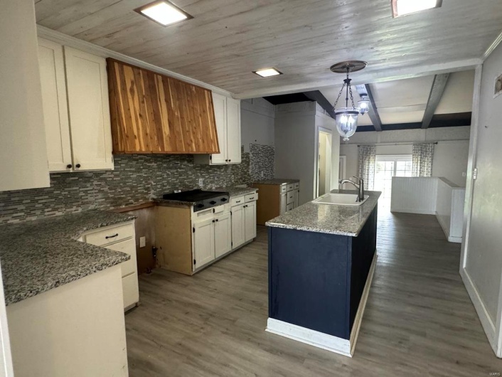 Kitchen with a sink, tasteful backsplash, a center island with sink, white cabinets, and wood finished floors