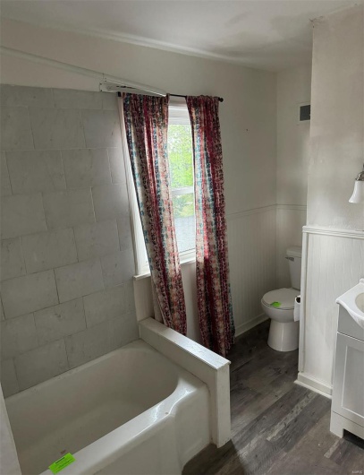Full bath with toilet, a bathtub, wood finished floors, a wainscoted wall, and vanity