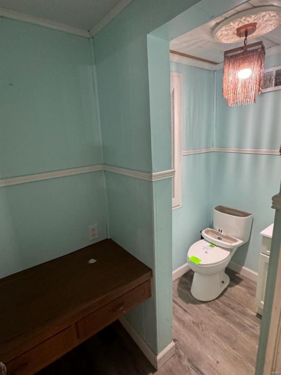 Half bathroom with wood finished floors, toilet, ornamental molding, and baseboards