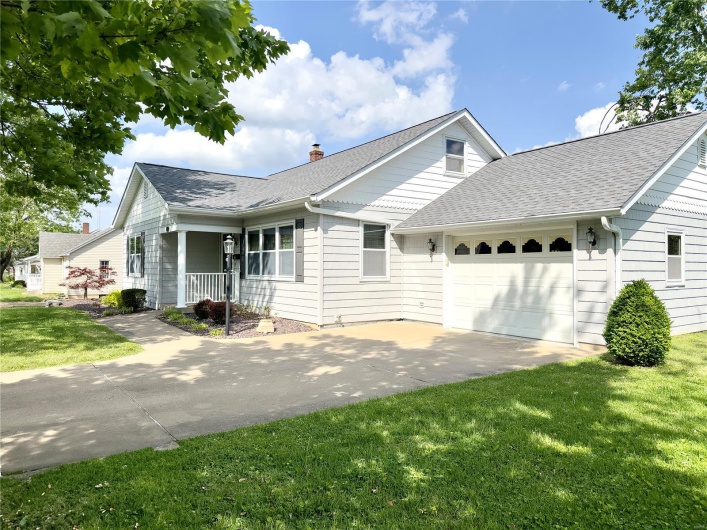 View of front of house featuring roof with shingles, an attached garage, a front lawn, a chimney, and driveway